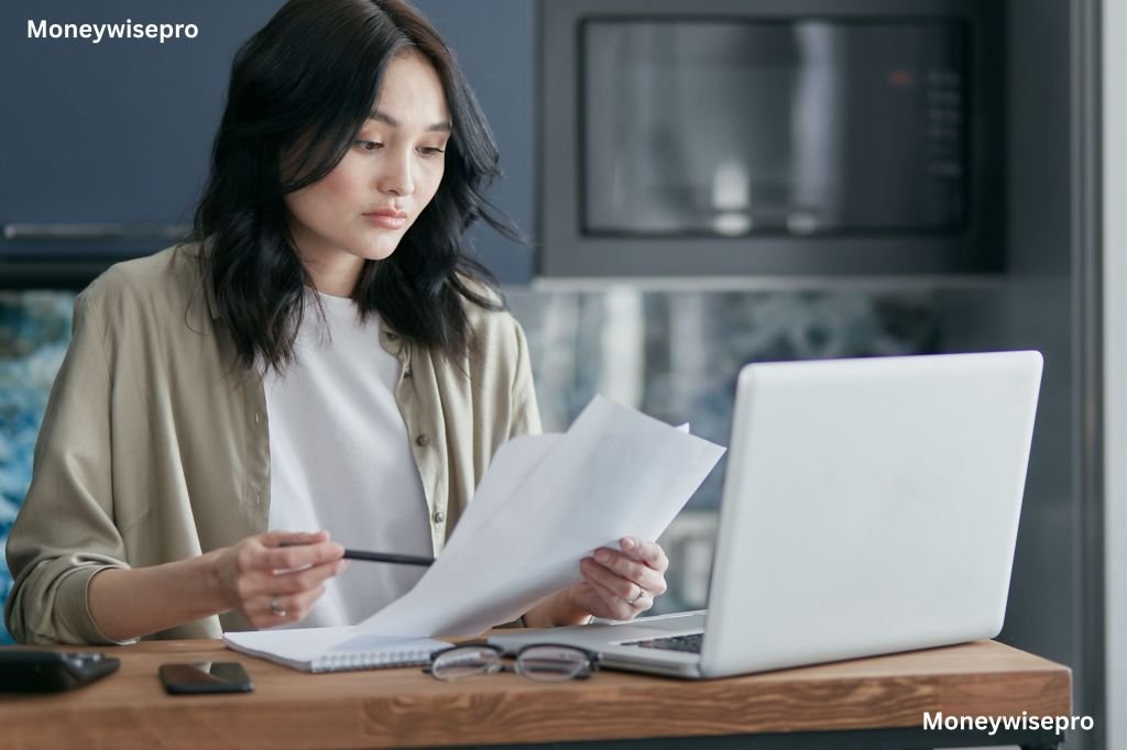 A woman in a gray cardigan comparing car insurance quotes on a laptop at her kitchen table