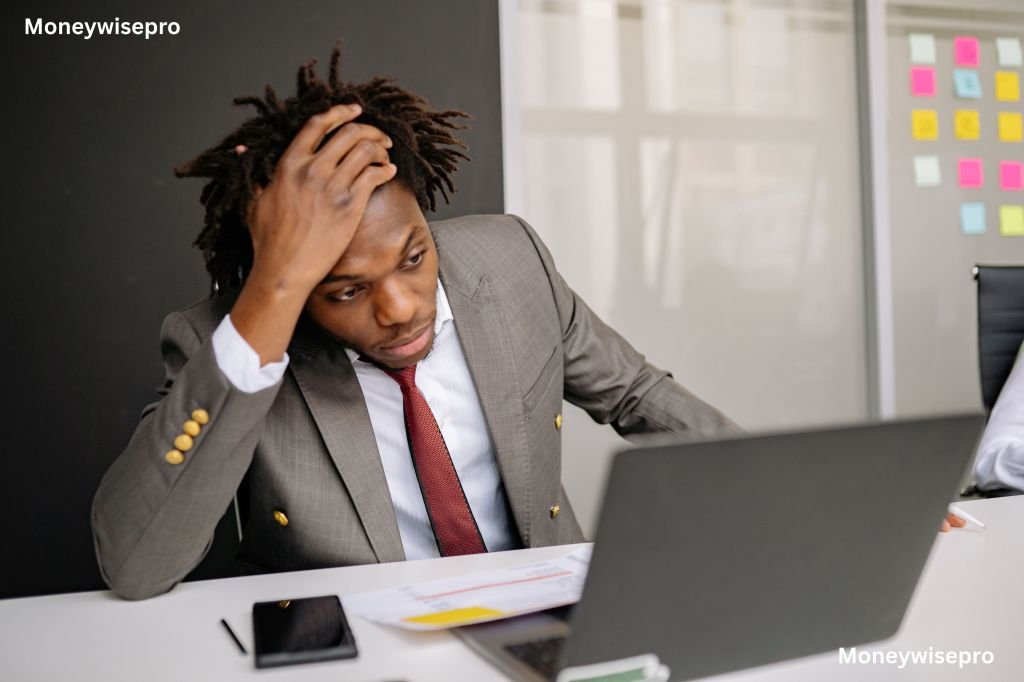  A young professional looking surprised while checking a paycheck on a laptop at a desk